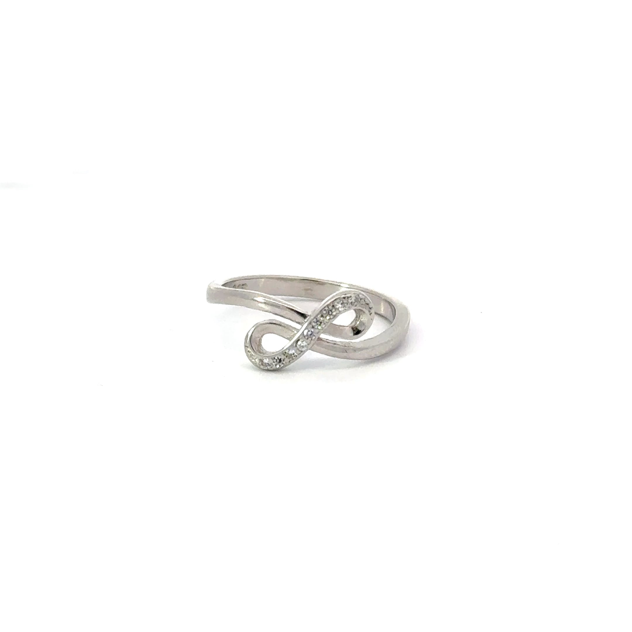 A white cubic zirconia sterling silver ring in an infinity shape design, with the ring positioned diagonally.