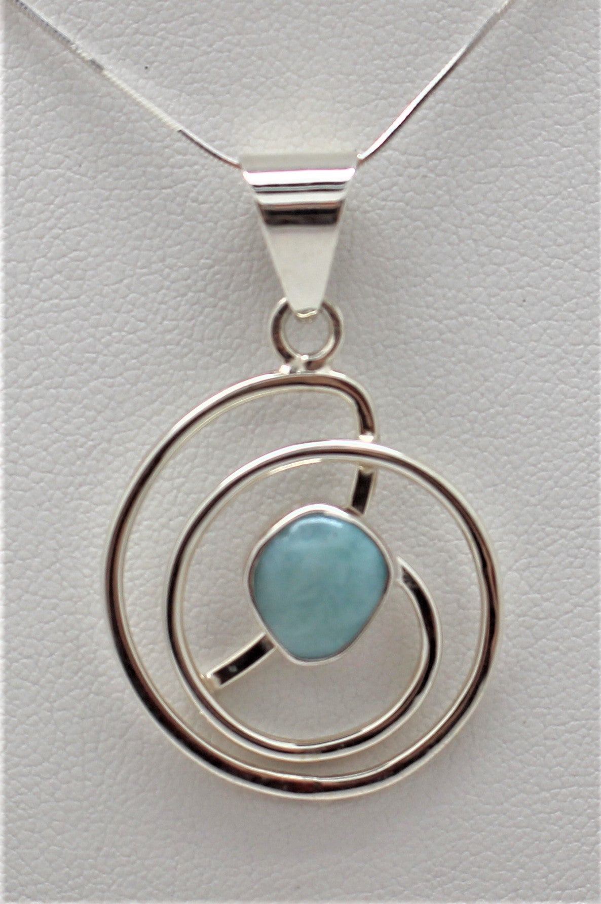 A Larimar Pendant set in a 925 Sterling Silver mounting, with a circular silver frame and a blue Larimar stone in the center.